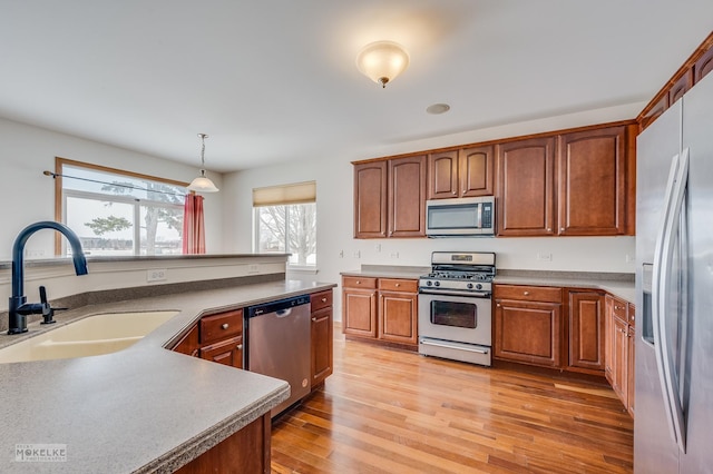 kitchen with sink, decorative light fixtures, stainless steel appliances, and light wood-type flooring