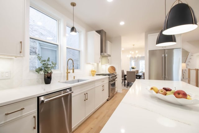 kitchen with hanging light fixtures, appliances with stainless steel finishes, wall chimney range hood, and white cabinets