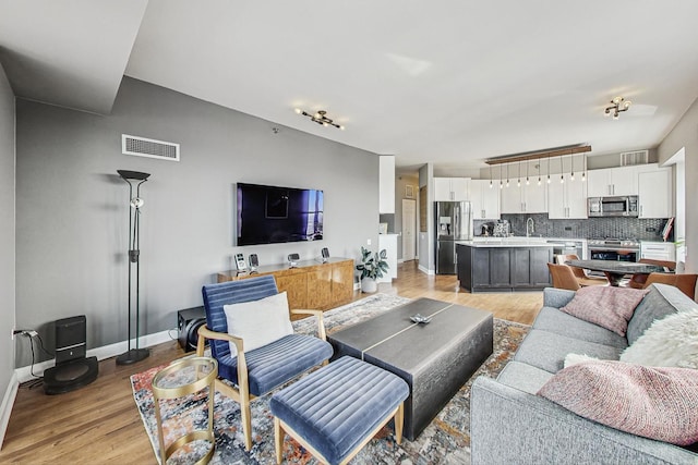 living area with light wood-style flooring, visible vents, and baseboards