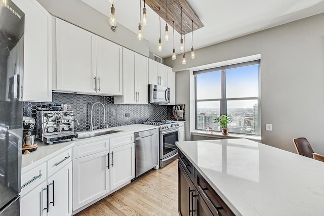 kitchen with backsplash, light wood-style flooring, appliances with stainless steel finishes, white cabinets, and a sink