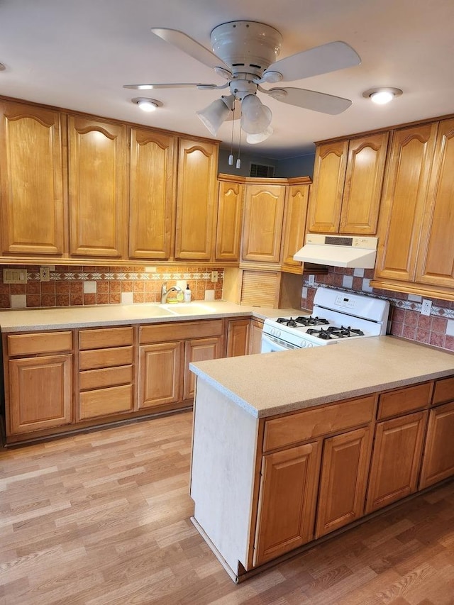 kitchen featuring white gas range, sink, decorative backsplash, and light hardwood / wood-style flooring