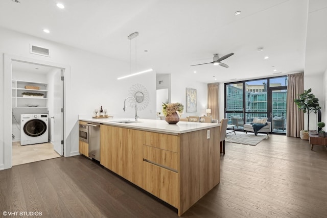 kitchen with dark wood-type flooring, sink, hanging light fixtures, expansive windows, and washer / clothes dryer