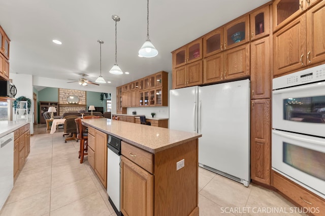 kitchen featuring a center island, hanging light fixtures, light tile patterned floors, white appliances, and light stone countertops