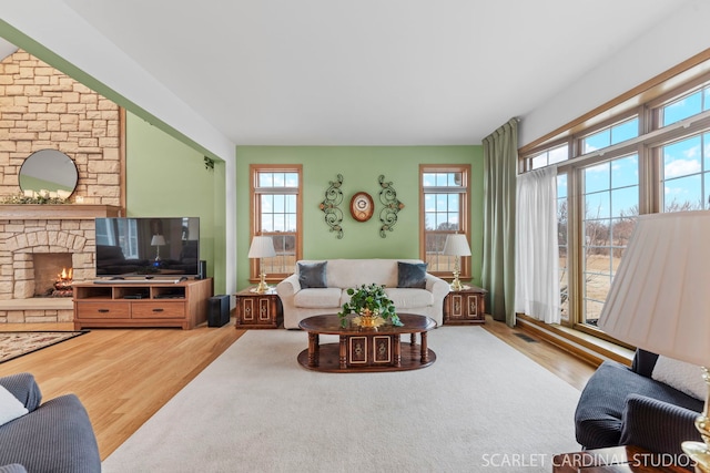 living room featuring a stone fireplace, wood-type flooring, and a wealth of natural light