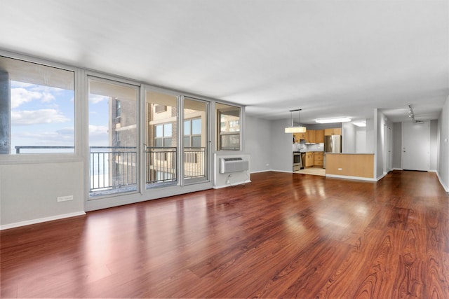 unfurnished living room featuring a wall mounted air conditioner, wood finished floors, and baseboards