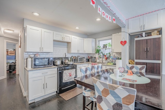 kitchen featuring gas range, white cabinetry, dark hardwood / wood-style floors, and decorative backsplash