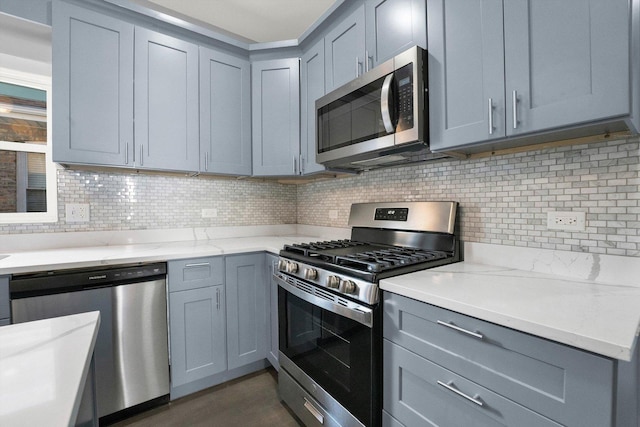 kitchen featuring gray cabinetry, appliances with stainless steel finishes, dark hardwood / wood-style flooring, light stone countertops, and decorative backsplash