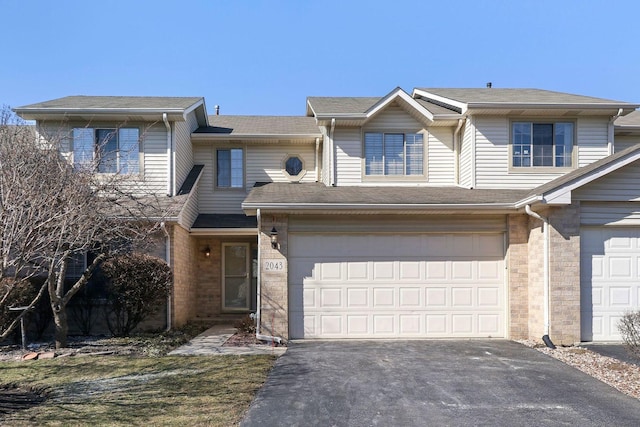 view of property featuring brick siding, an attached garage, aphalt driveway, and roof with shingles