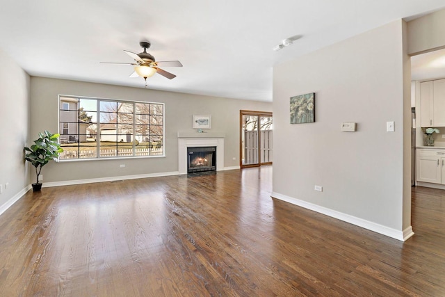 unfurnished living room featuring a wealth of natural light, a fireplace with flush hearth, dark wood finished floors, and baseboards