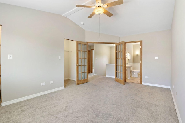 unfurnished bedroom featuring a walk in closet, carpet floors, vaulted ceiling, french doors, and ensuite bath