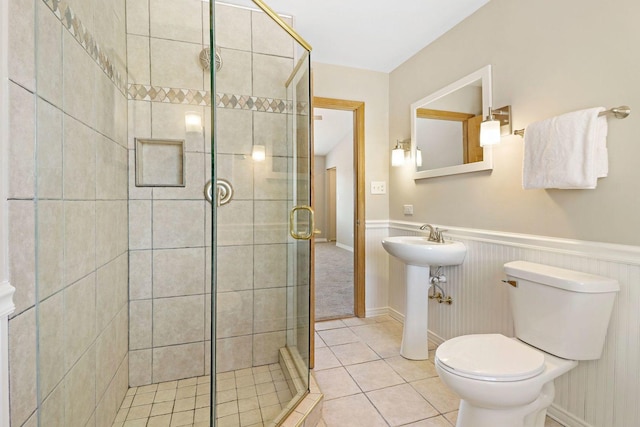 bathroom featuring tile patterned floors, a wainscoted wall, a shower stall, and toilet