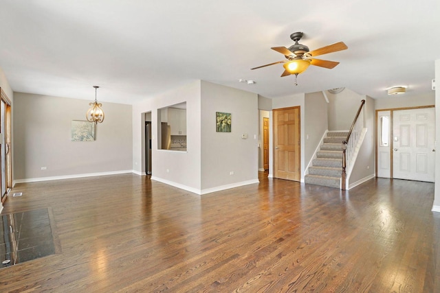 unfurnished living room with stairway, baseboards, dark wood-style floors, and ceiling fan with notable chandelier