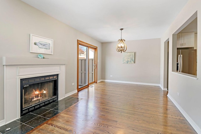 unfurnished living room featuring a chandelier, a fireplace with flush hearth, baseboards, and wood finished floors