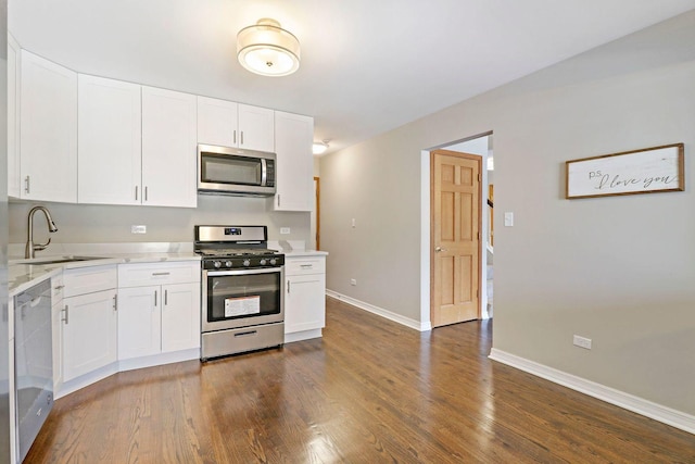 kitchen with baseboards, a sink, stainless steel appliances, dark wood-type flooring, and white cabinets