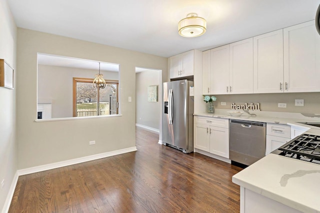 kitchen with pendant lighting, dark wood finished floors, white cabinetry, appliances with stainless steel finishes, and baseboards