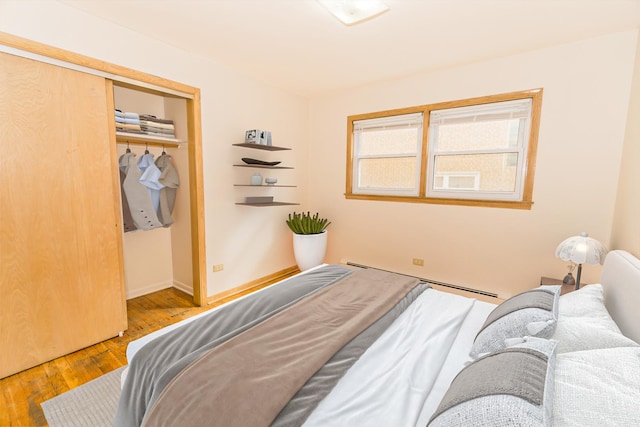 bedroom featuring a baseboard heating unit, a closet, and light wood-type flooring