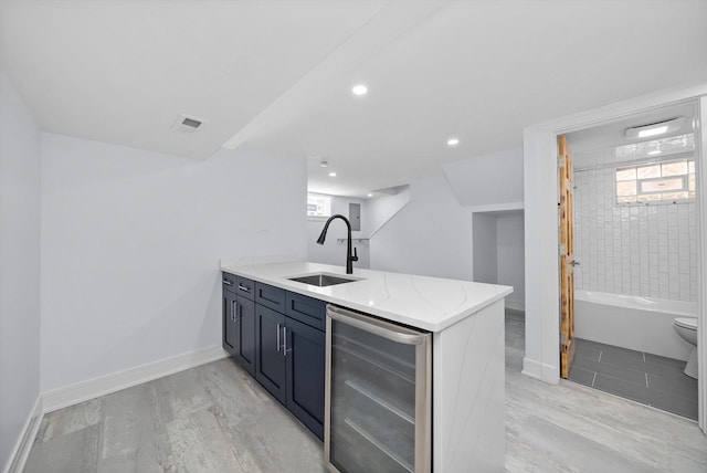 kitchen with wine cooler, sink, kitchen peninsula, light stone countertops, and light hardwood / wood-style floors