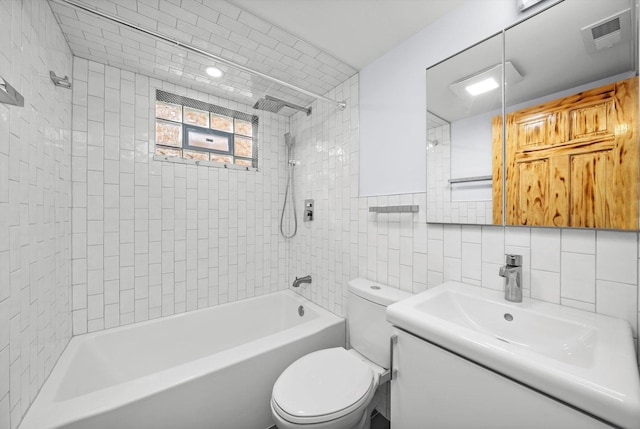 full bathroom featuring tiled shower / bath, vanity, toilet, and tile walls