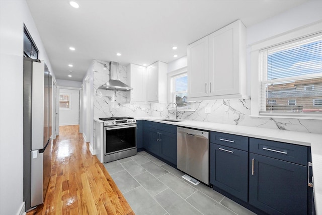 kitchen featuring sink, blue cabinetry, appliances with stainless steel finishes, white cabinets, and wall chimney exhaust hood