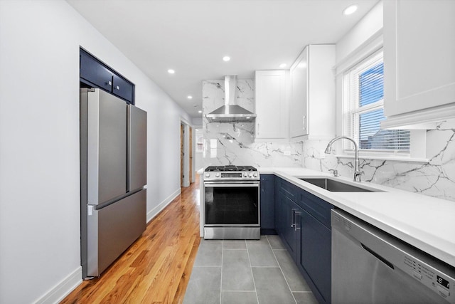 kitchen with blue cabinetry, sink, wall chimney range hood, stainless steel appliances, and white cabinets