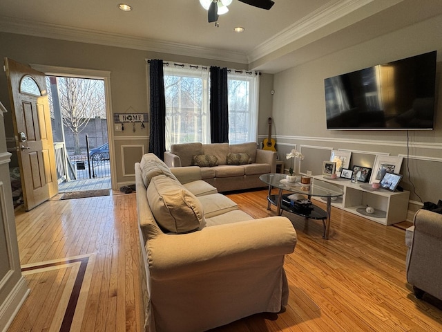 living room featuring light wood finished floors, a decorative wall, wainscoting, and crown molding