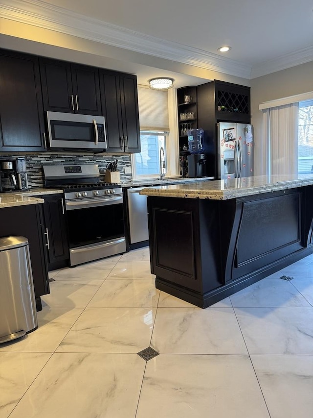 kitchen featuring stainless steel appliances, ornamental molding, dark cabinets, and light stone countertops