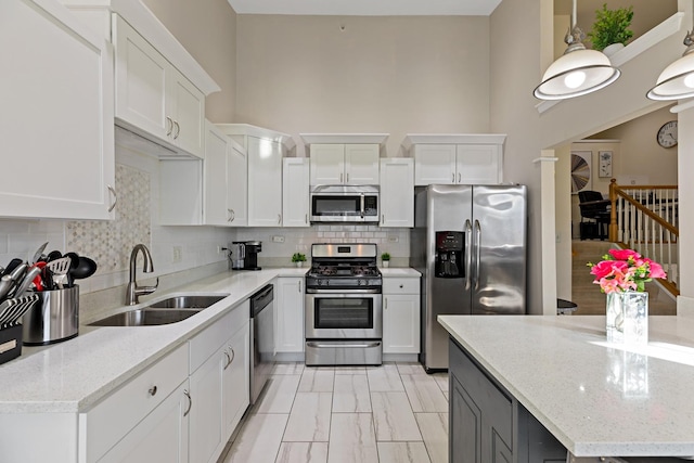 kitchen featuring sink, appliances with stainless steel finishes, white cabinetry, hanging light fixtures, and light stone countertops