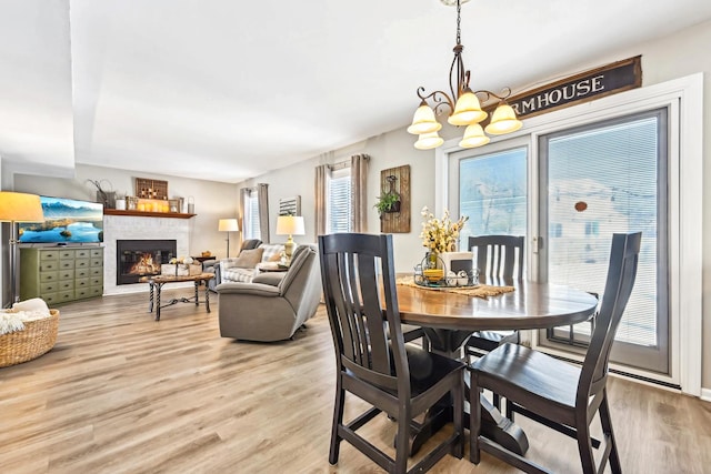 dining space with light wood-type flooring, a glass covered fireplace, a healthy amount of sunlight, and an inviting chandelier