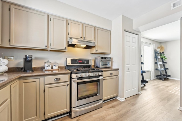 kitchen featuring dark countertops, visible vents, light wood-style flooring, stainless steel gas range, and under cabinet range hood