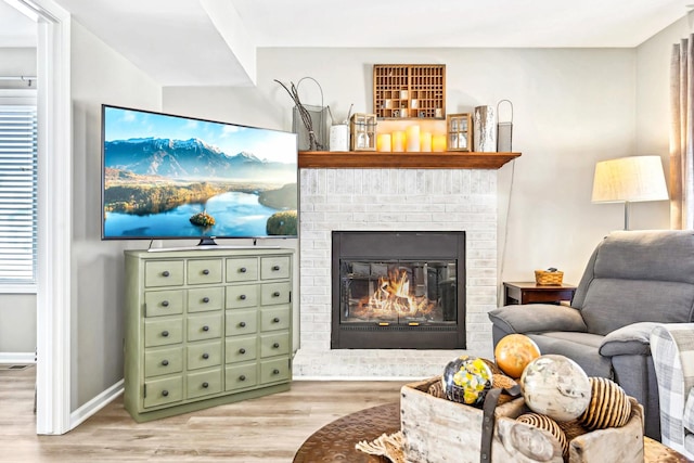 living area with light wood finished floors, a brick fireplace, and baseboards