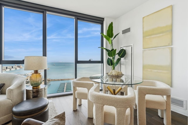 dining space with floor to ceiling windows, a water view, visible vents, a healthy amount of sunlight, and wood finished floors