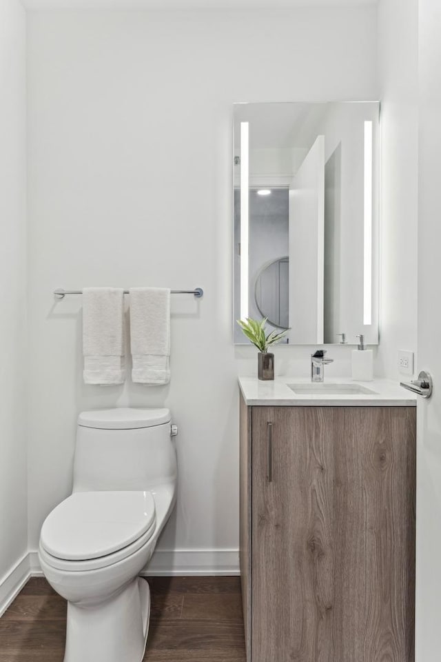 half bath featuring baseboards, wood finished floors, and vanity