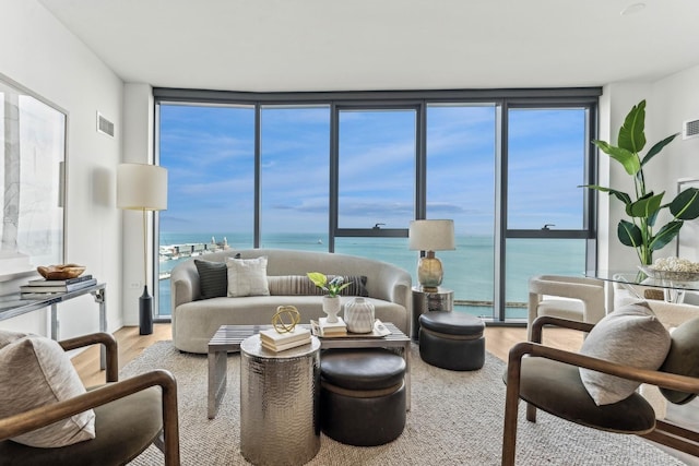 living area featuring a water view, light wood-style flooring, visible vents, and a wall of windows