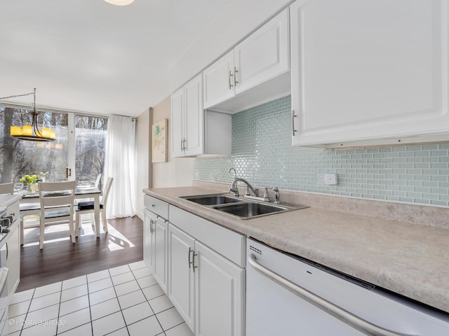 kitchen with light tile patterned floors, decorative backsplash, white cabinetry, white dishwasher, and a sink