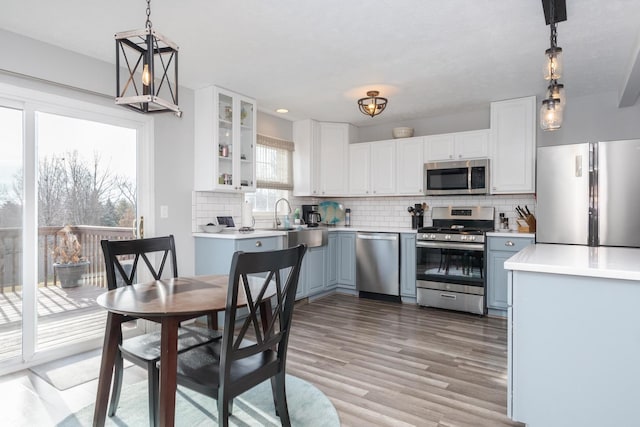 kitchen with appliances with stainless steel finishes, pendant lighting, sink, white cabinets, and light wood-type flooring