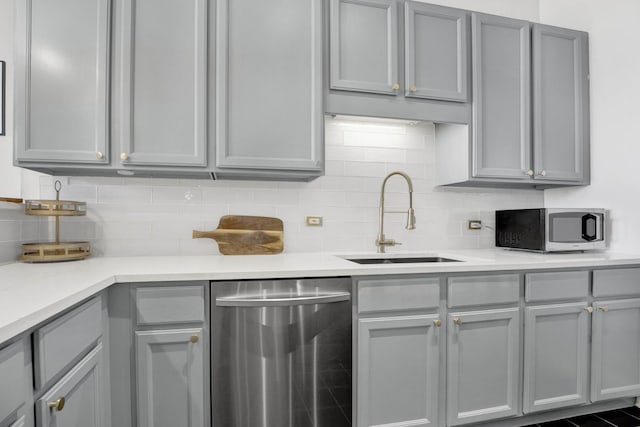 kitchen with tasteful backsplash, appliances with stainless steel finishes, sink, and gray cabinetry