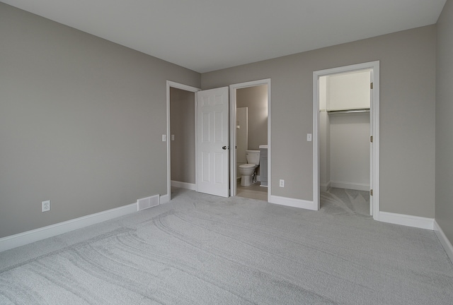 unfurnished bedroom with connected bathroom, a spacious closet, and light colored carpet