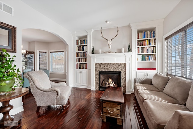 living area with built in shelves, a tile fireplace, dark wood finished floors, and visible vents