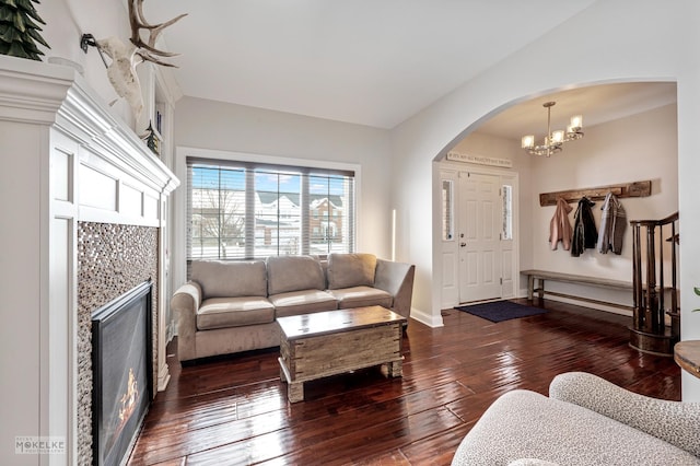 living room featuring arched walkways, dark wood finished floors, a chandelier, a lit fireplace, and baseboards