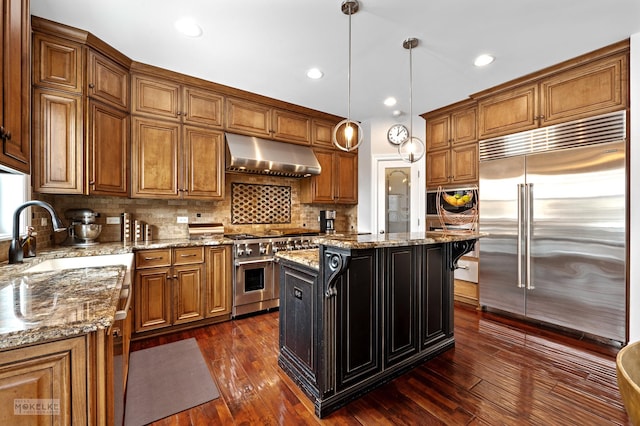 kitchen with a center island, decorative light fixtures, high end appliances, light stone countertops, and extractor fan