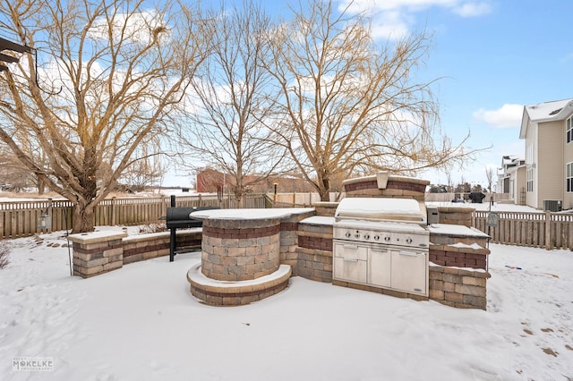 snow covered patio featuring exterior kitchen, a fenced backyard, and grilling area