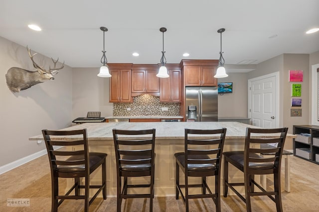 kitchen featuring decorative backsplash, brown cabinetry, a spacious island, a breakfast bar area, and stainless steel refrigerator with ice dispenser