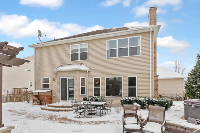 snow covered house with a hot tub, fence, and a chimney