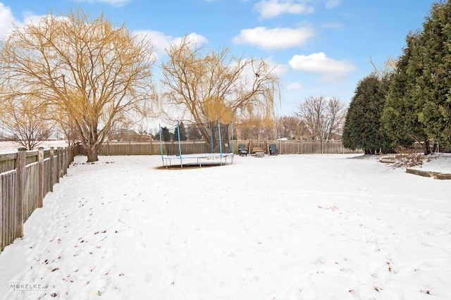 yard covered in snow with a fenced backyard and a trampoline