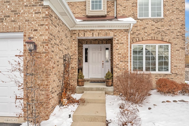 snow covered property entrance featuring a garage and brick siding