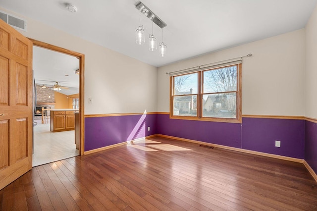 empty room with wood-type flooring, visible vents, ceiling fan, and baseboards