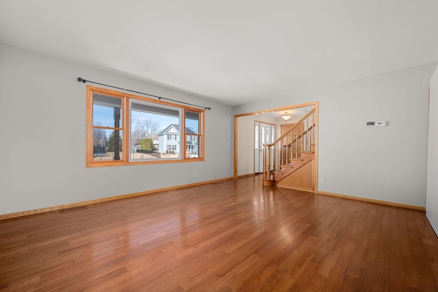 unfurnished room featuring stairs, wood-type flooring, visible vents, and baseboards