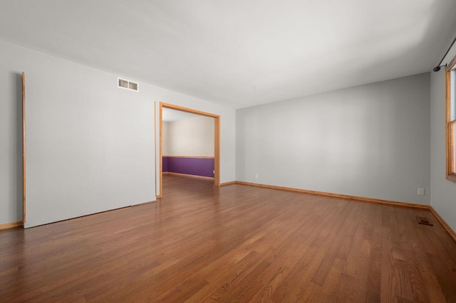 empty room featuring wood finished floors, visible vents, and baseboards