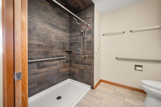 bathroom featuring toilet, baseboards, and a tile shower