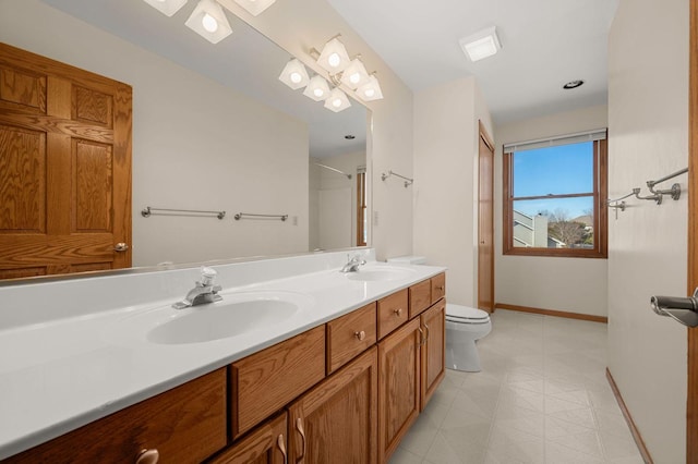 full bathroom featuring double vanity, a sink, toilet, and baseboards